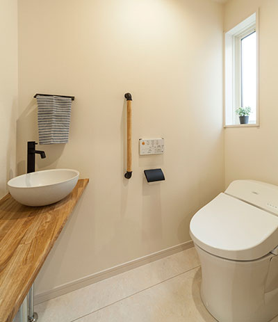 白い床と白い壁のトイレ。木のカウンターがあり、手洗いには白い水栓ボウルが設置されている