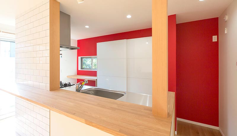 アイランドタイプのキッチンスペース。キッチンの壁やキッチン収納はホワイト、対照的にキッチン背面の壁はビビットな赤色のアクセント壁。