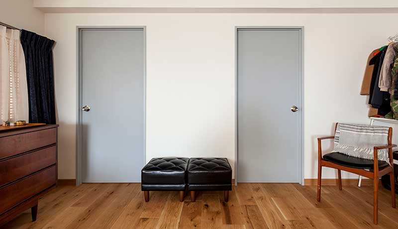 白い壁に対照的に並ぶドア。ドアとドアの間には黒いスツールが2つ並んでいる