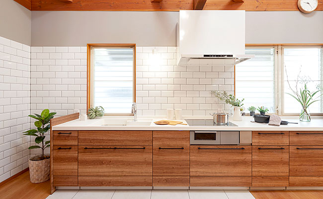 Ｔ字に配置されたセパレートキッチンと大工製作のダイニングテーブル。キッチン背面の壁の一部には、マンションのの外部で使用されているタイルと同一のタイルをアクセントに貼っている