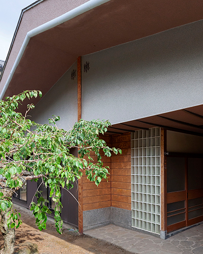 グレーの壁の外観には、木やガラスブロックをアクセントに使用している。