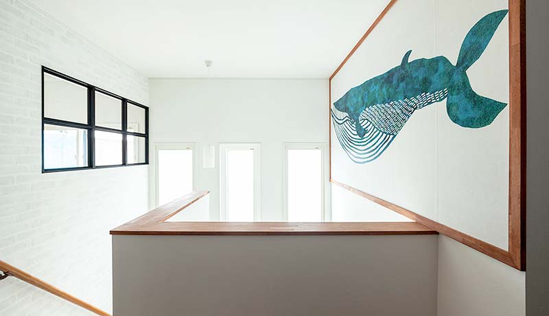 窓から光を採り込んだ明るい階段の吹抜け空間。２階の壁の一部に大きなクジラを描いた壁紙が貼られている