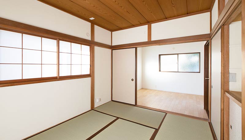 白い壁の和室スペース。左側には腰窓があり障子戸が取り付けられている。和室の奥隣には白い襖で仕切れるフローリングスペースがある