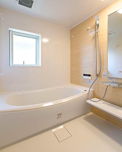 バスルームの写真。ユニットバスで白い天井と壁と床、そして白い浴槽があり、鏡のある一面の壁だけ木目調のパネルとなっている